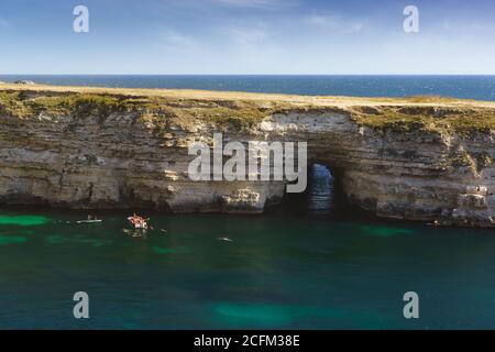 Tarhankut, Crimea, Russia - 11 settembre 2019: I turisti nuotano vicino alla grotta del tunnel di Chuch nella costa rocciosa della penisola di Tarhankut Foto Stock