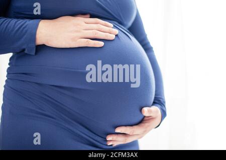 Donna incinta in abito blu tiene la sua pancia bump. Foto luminosa su sfondo bianco Foto Stock