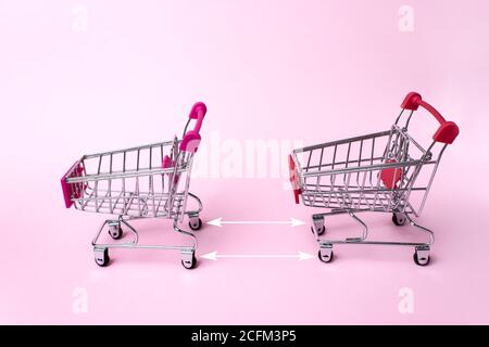 Carrelli per lo shopping dal supermercato su sfondo rosa chiaro con frecce che indicano la distanza tra i carrelli in negozio. Due vuoti in acciaio inox piccolo Foto Stock