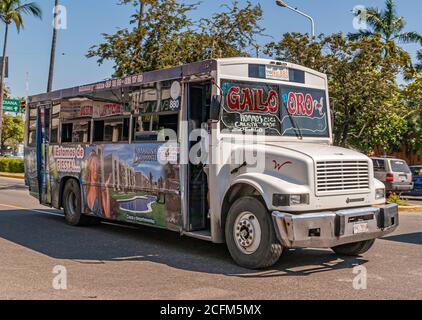 Acapulco, Messico - 25 novembre 2008: Centro storico. Autobus pubblico bianco per passeggeri con pubblicità colorate in tutta la strada con fogliame verde in b Foto Stock