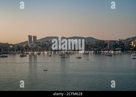 Acapulco, Messico - 25 novembre 2008: Twilihgt sopra la baia blu dell'acqua con il porto degli yacht e gli edifici alti lungo il litorale con l'alto edificio Foto Stock