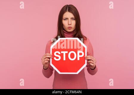 Preoccupata donna che tiene il segno di stop nelle mani, avvertendo circa il rispetto delle regole, le leggi sulla circolazione. Studio al coperto isolato su sfondo rosa Foto Stock
