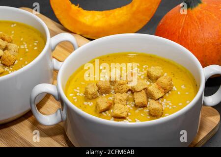 Zuppa di zucca autunnale con semi di sesamo su sfondo ligneo. Primo piano di zuppa di zucca vegetariana arancione con cracker Foto Stock