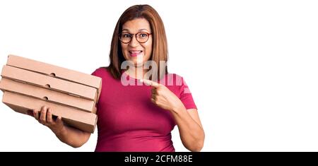 Donna latina di mezza età che tiene la scatola della pizza di consegna sorridente felice puntare con la mano e il dito Foto Stock