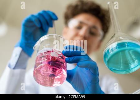 Guanto le mani del ricercatore con una pipetta che prende un po' di liquido rosa sostanza Foto Stock