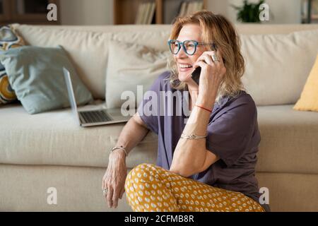 Donna bionda matura felice in casualwear seduto sul pavimento da lettino Foto Stock
