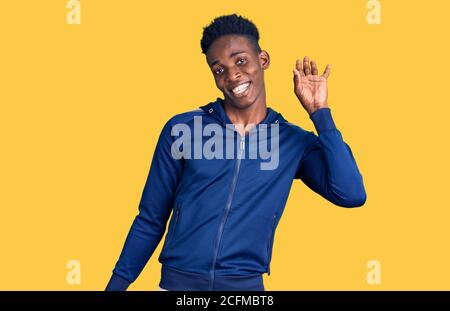 Giovane afroamericano che indossa una vita sportiva dicendo ciao felice e sorridente, amichevole gesto di benvenuto Foto Stock