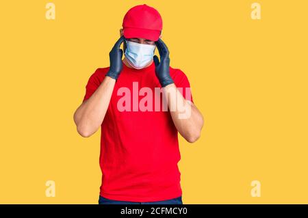 Giovane uomo ispanico che indossa covid-19 maschera di sicurezza che soffre di mal di testa disperato e stressato perché dolore ed emicrania. Mani sulla testa. Foto Stock