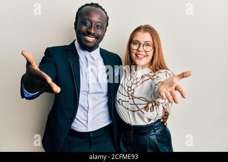 Giovane coppia interracial che indossa gli affari e i vestiti eleganti sorridente amichevole che offre handshake come saluto e accogliente. Business di successo. Foto Stock