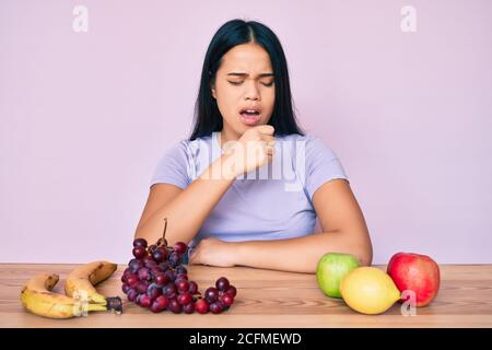 Giovane bella ragazza asiatica mangiare frutta fresca e sana sensazione di malessere e tosse come sintomo di freddo o bronchite. Concetto di assistenza sanitaria. Foto Stock