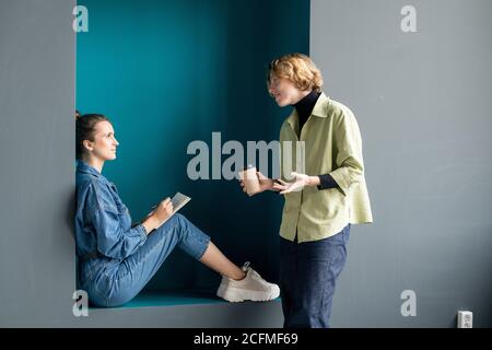 Due giovani donne d'affari contemporanee in casualwear che discutono di lavoro in ufficio Foto Stock