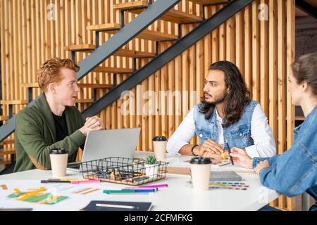 Tre giovani sviluppatori istruiti di software che discutono le loro idee a. riunione Foto Stock