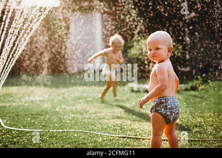 Bambini piccoli che giocano con l'acqua dell'irrigatore nel cortile Foto Stock