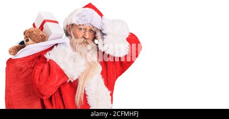 Vecchio uomo anziano con capelli grigi e barba lunga che indossa babbo natale borsa di tenuta costume con regali stressati e frustrati con mano sulla testa, sorpresa Foto Stock