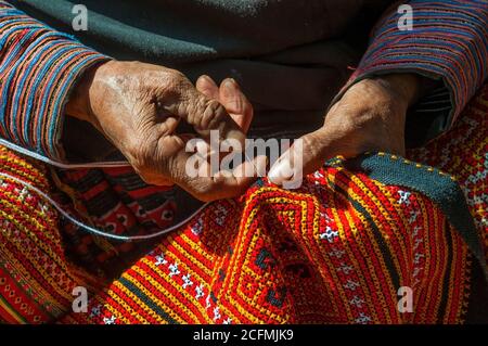 Mani di una donna Hmong nero cucire tessuto tradizionale colorato e altre arti e mestieri con le mani alla luce del sole, Vietnam del Nord. Foto Stock