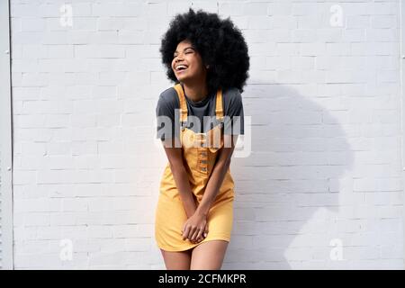 Donna africana felice con capelli afro che ride in piedi contro muro di mattoni bianchi. Foto Stock