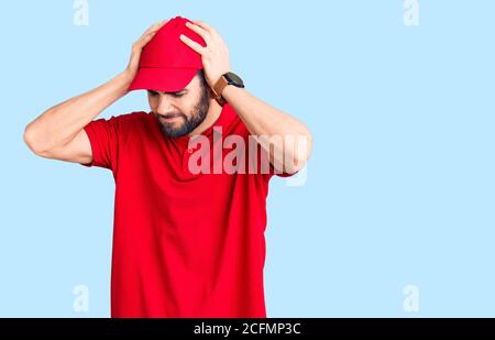 Giovane bell'uomo con barba che indossa la consegna uniforme che soffre di mal di testa disperato e stressato a causa del dolore e l'emicrania. Mani sulla testa. Foto Stock