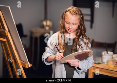 Uno studente di una scuola d'arte mescola colori su una tavolozza per il suo disegno di tela in un laboratorio Foto Stock