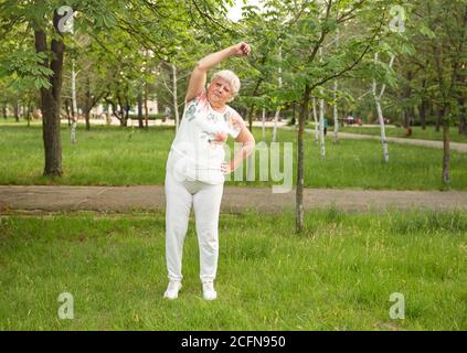 La donna anziana sta facendo lo yoga e l'esercitazione di stretching in parcheggio Foto Stock