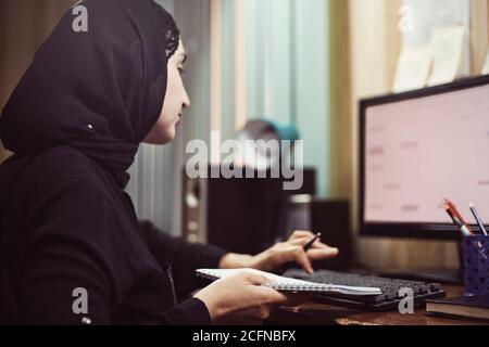 Imprenditore femminile medio-orientale. Bussata donna d'affari araba. Una donna di mezza età in abiti tradizionali arabi hijab o abaya che lavora su PC Foto Stock