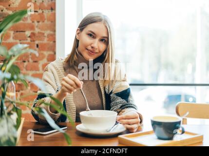 Giovane donna bionda sorridente in abbigliamento casual con pranzo a. il caffè Foto Stock