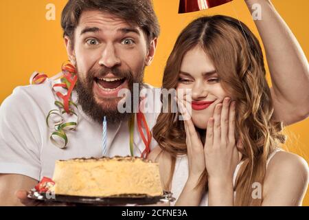 Uomo e donna compleanno festa torta sfondo giallo e cappelli sulla headv Foto Stock