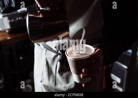 Barista mani versando il latte caldo in una tazza da caffè per preparare latte art. Primo piano Foto Stock