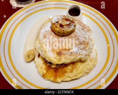 Frittelle di banana senza glutine - banana cotta a fette servita in cima a pancake. Servito con una tazza di sciroppo d'acero. Popolare ristorante informale americano. Foto Stock