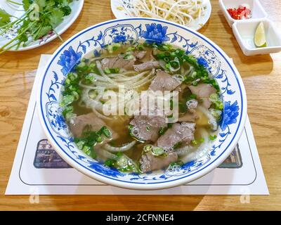 Pho Bo, una zuppa vietnamita composta da brodo, tagliatelle di riso, erbe e manzo. Popolare cibo di strada in Vietnam. Aggiunta di salsa variabile. Foto Stock