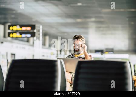 Un uomo caucasico adulto lavora a un computer portatile che lo aspetta volo al cancello dell'aeroporto - concetto di nomade digitale e tecnologia relativa al lavoro - pe moderno Foto Stock