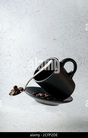 messa a fuoco selettiva, tazza da caffè volante, con piattino e chicchi di caffè su sfondo chiaro Foto Stock