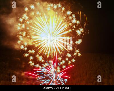 Due luminosi lampi di fuochi d'artificio in oro e blu colore con color cremisi scintilla sullo sfondo di un buio foresta nella foschia Foto Stock