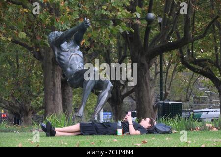 Melbourne Australia. Scene di vita quotidiana a Melbourne Australia . Leggere il telefono mentre si trova in un parco sotto la 'Hammer Thrower Sculpture ' Foto Stock