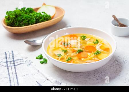Zuppa di pollo fatta in casa con tagliatelle e verdure in una ciotola bianca, fondo bianco. Cibo sano, caldo e confortevole. Foto Stock