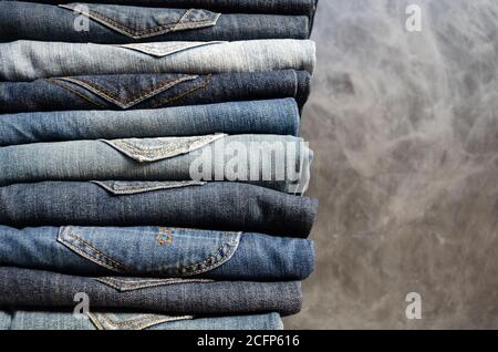 Una pila di jeans perfettamente ripiegati su sfondo grigio. Primo piano di jeans in diversi colori. Texture jeans o sfondo in denim. Spazio di copia Foto Stock