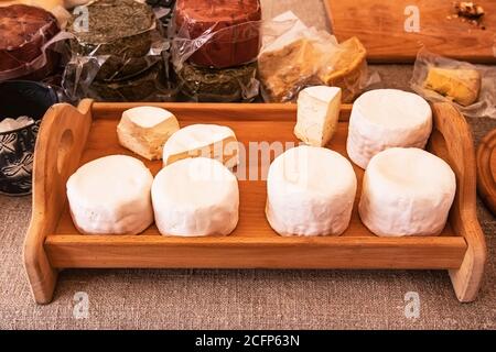 Teste rotonde di camembert bianco e formaggio brie su un vassoio di legno vicino a pacchetti di formaggi artigianali assortiti in una fiera degli agricoltori. Fattoria casalinga chee sano Foto Stock
