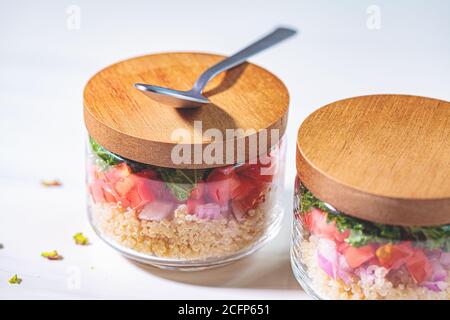 Insalata vegana con verdure e quinoa in vasetti di vetro, fondo bianco. Takeaway, cibo vegetariano sano, concetto zero rifiuti. Foto Stock