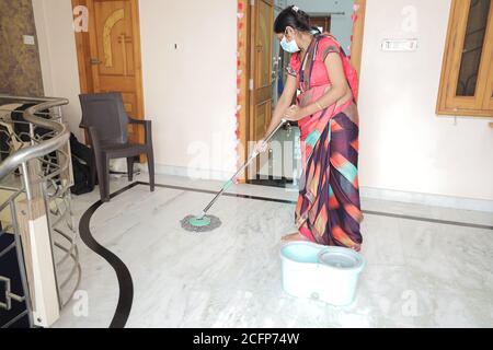 Donna indiana che indossa maschera piano di pulizia con spazzolone igienizzante. Pavimento di pulizia a casa, protezione contro covid-19 / coronavirus, igiene della casa e Clea Foto Stock