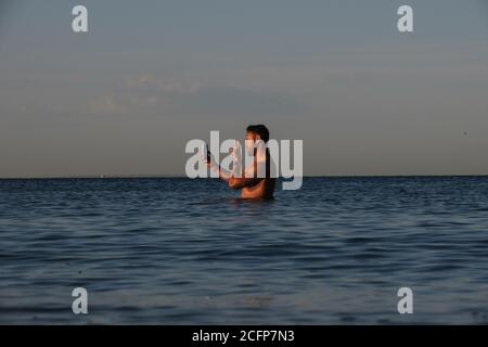 Melbourne Australia; parlare al telefono mentre si è in vita in acqua. Un uomo usa il suo telefono mentre si trova nella baia di Port Phillip. Foto Stock