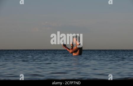 Melbourne Australia; parlare al telefono mentre si è in vita in acqua. Un uomo usa il suo telefono mentre si trova nella baia di Port Phillip. Foto Stock