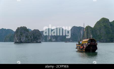 Cat Ba, Vietnam - 19 Novembre 2019 : Barca spazzatura che naviga in LAN ha Bay vicino ha Long Bay, carsica di montagna in background, mare, cielo sovrastato. Foto Stock