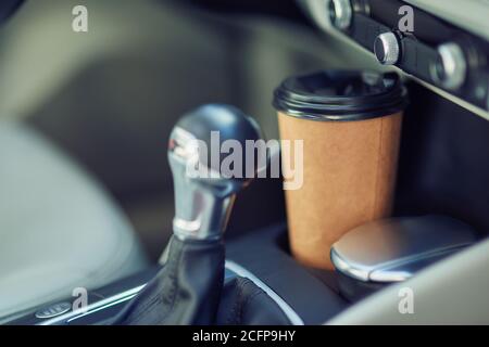 Primo piano di una tazza di caffè in carta il portabicchieri tra i sedili di un'auto moderna Foto Stock