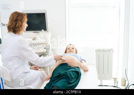 Il medico femminile esamina l'addome della pancia della giovane donna incinta sdraiata Foto Stock