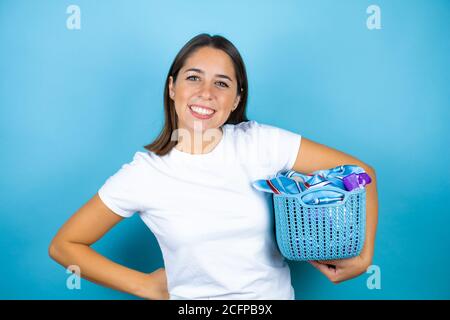 Giovane bella donna su sfondo blu isolato facendo housewwork tenendo un cestino con i vestiti Foto Stock