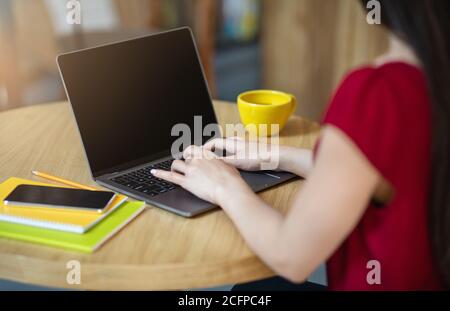 Donna irriconoscibile che scrive sul laptop con schermo nero in caffetteria, immagine mockup Foto Stock