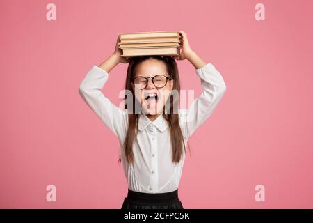 La bambina con gli occhiali tiene la pila dei libri su lei testa e grida Foto Stock