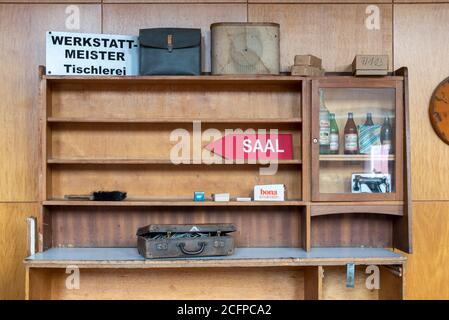04 settembre 2020, Sassonia-Anhalt, Magdeburgo: In una mensola di legno si trova un cartello con la chiamata Werkstatt-Meister Tischlerei. Accanto c'è una borsa e un vecchio altoparlante, sotto di essa una valigia. Gli oggetti appartengono all'inventario dello Stadthalle, che sono venduti completamente. L'edificio sarà poi rinnovato entro tre anni. Costi: Circa 70 milioni di euro. L'edificio è stato costruito tra il 1926 e il 1927 in occasione della mostra teatrale tedesca nello stile di Neues Bauen. Gli architetti furono Johannes Göderitz e Wilhelm Deffke. Foto: Stephan Schulz/dpa-Zentralbild/ZB Foto Stock