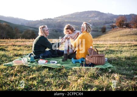 Bambina con madre e nonna che hanno pic-nic in natura al tramonto. Foto Stock