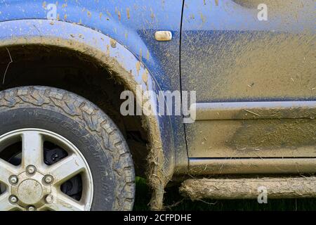 vista laterale parziale di un 4x4 blu e di tutti i terreni pneumatico frantumato con fango sporco fangoso che ha bisogno di un pulire Foto Stock