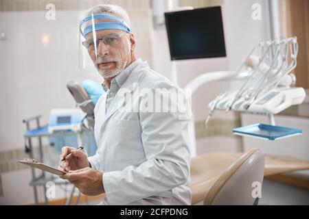 Specialista dentale competente che prende appunti sul lavoro Foto Stock